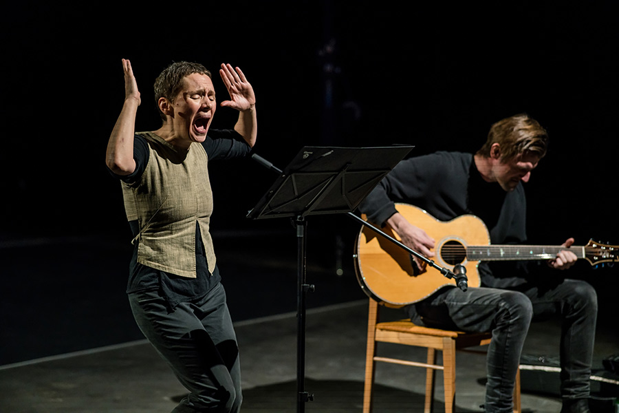 Eine singende Frau vor einem Mikro, daneben sitzt ein Mann, der Gitarre spielt